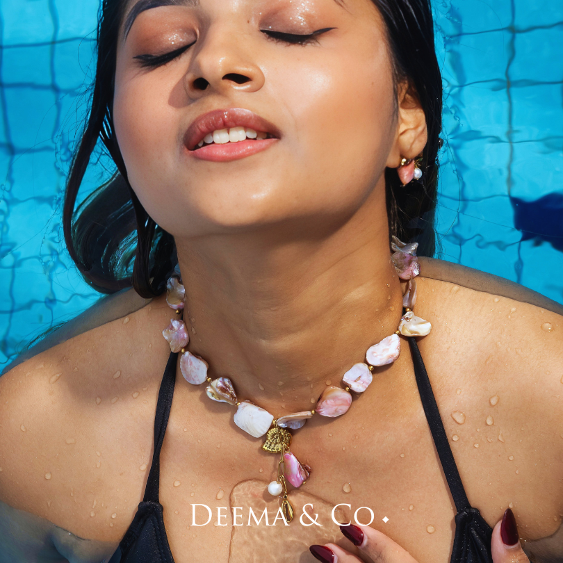Model wearing Deema & Co. permanent pink and white conch shell earrings and necklace with gold accents and pearl details - 18K Gold PVD conch shell earrings with pearls by Deema & Co. on model - waterproof tarnish free and hypoallergenic